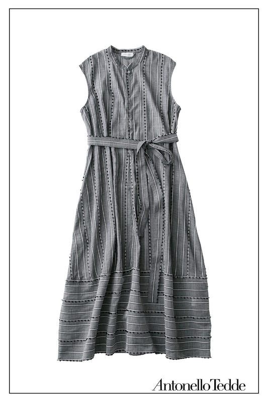 Grey sleeveless dress with a standing collar, crafted from 100% Khadi cotton handwoven in India and made in Italy, featuring a flowing design with pom detail and with hidden pockets and a matching belt for versatile styling.