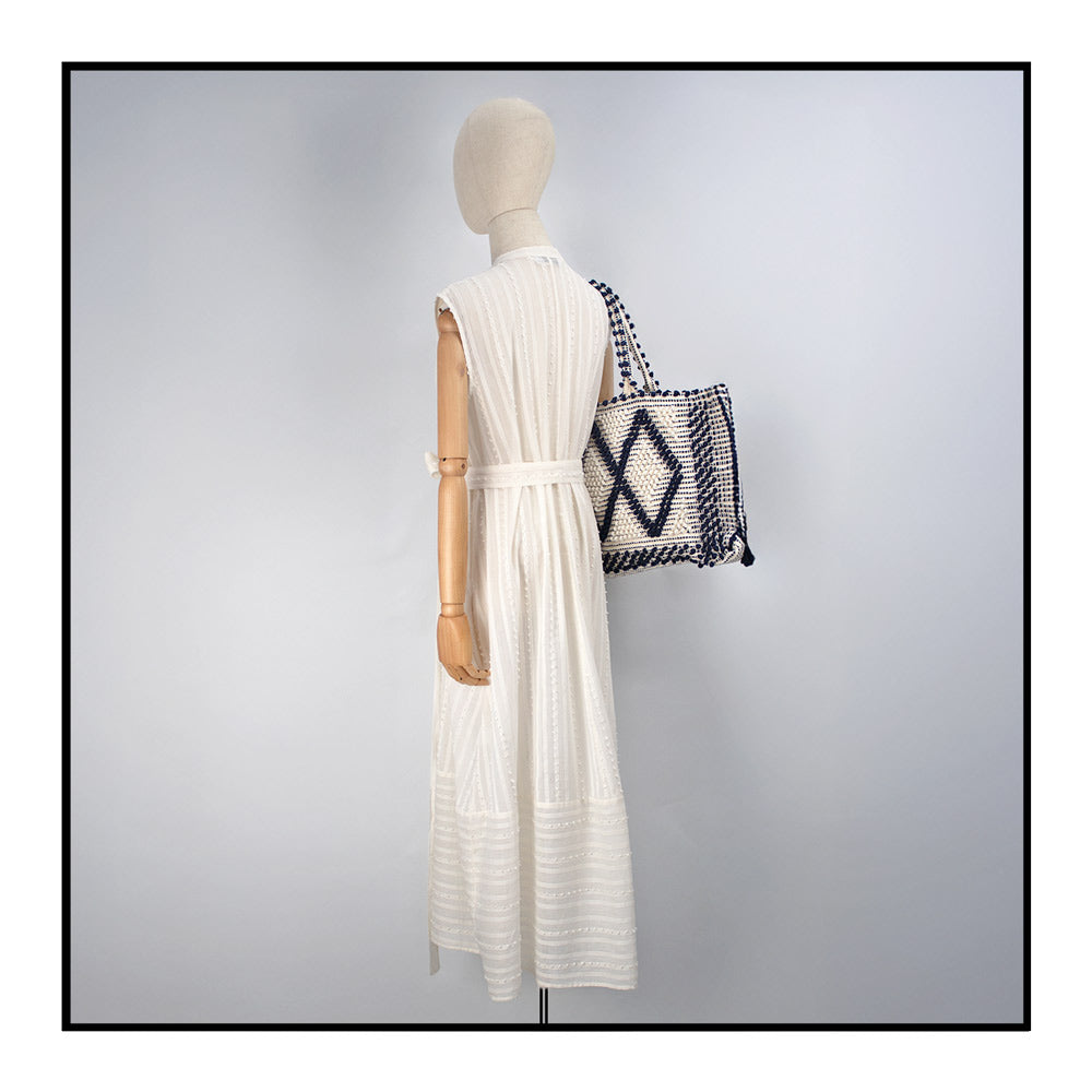 Cream sleeveless dress with a standing collar, crafted from 100% Khadi cotton handwoven in India, featuring a flowing design with hidden pockets and a matching belt for versatile styling. Paired here with a black and cream tote  from Antonello Tedde collection. 