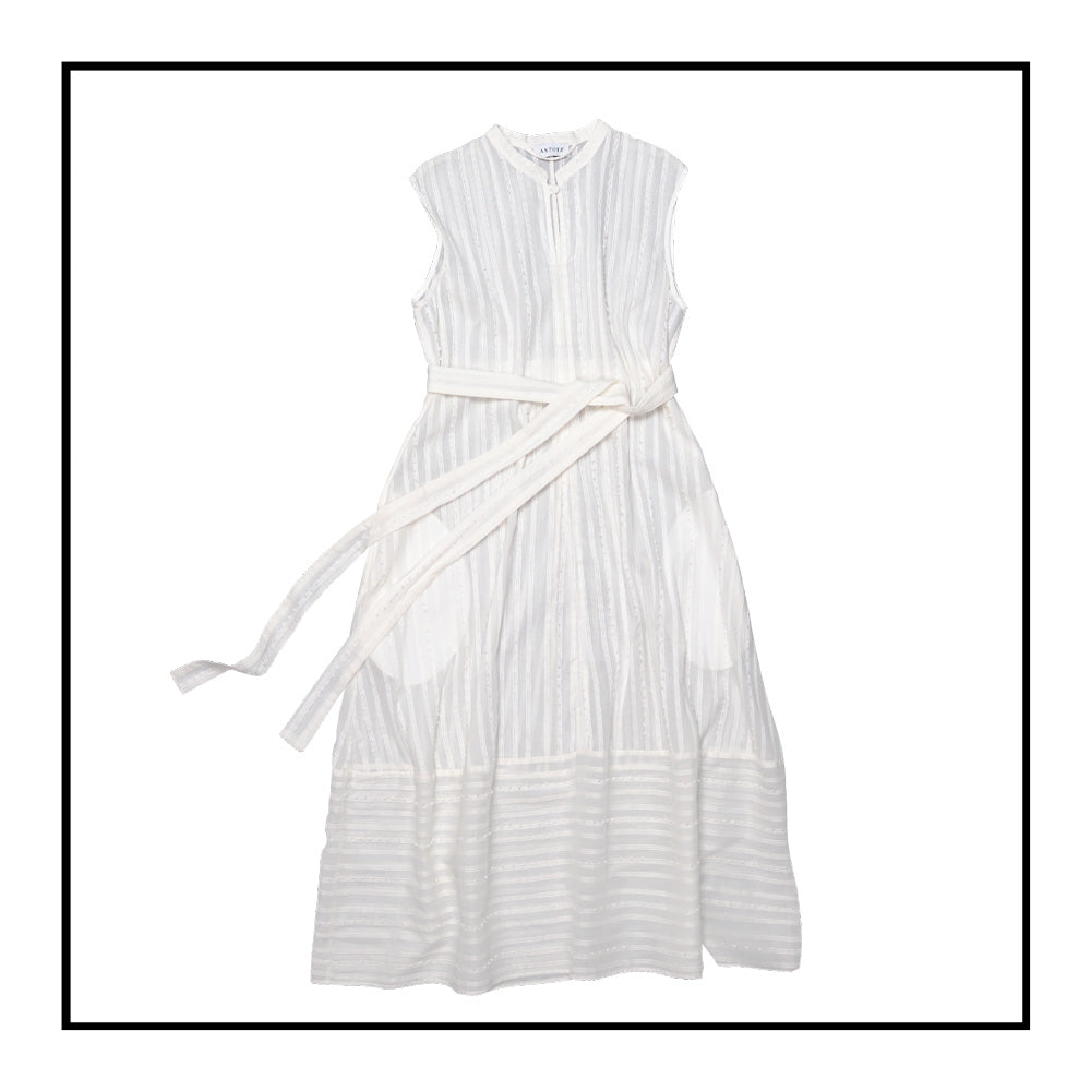 A cream sleeveless dress with a standing collar, crafted from 100% Khadi cotton handwoven in India, features a flowing design with hidden pockets and a matching belt for versatile styling.