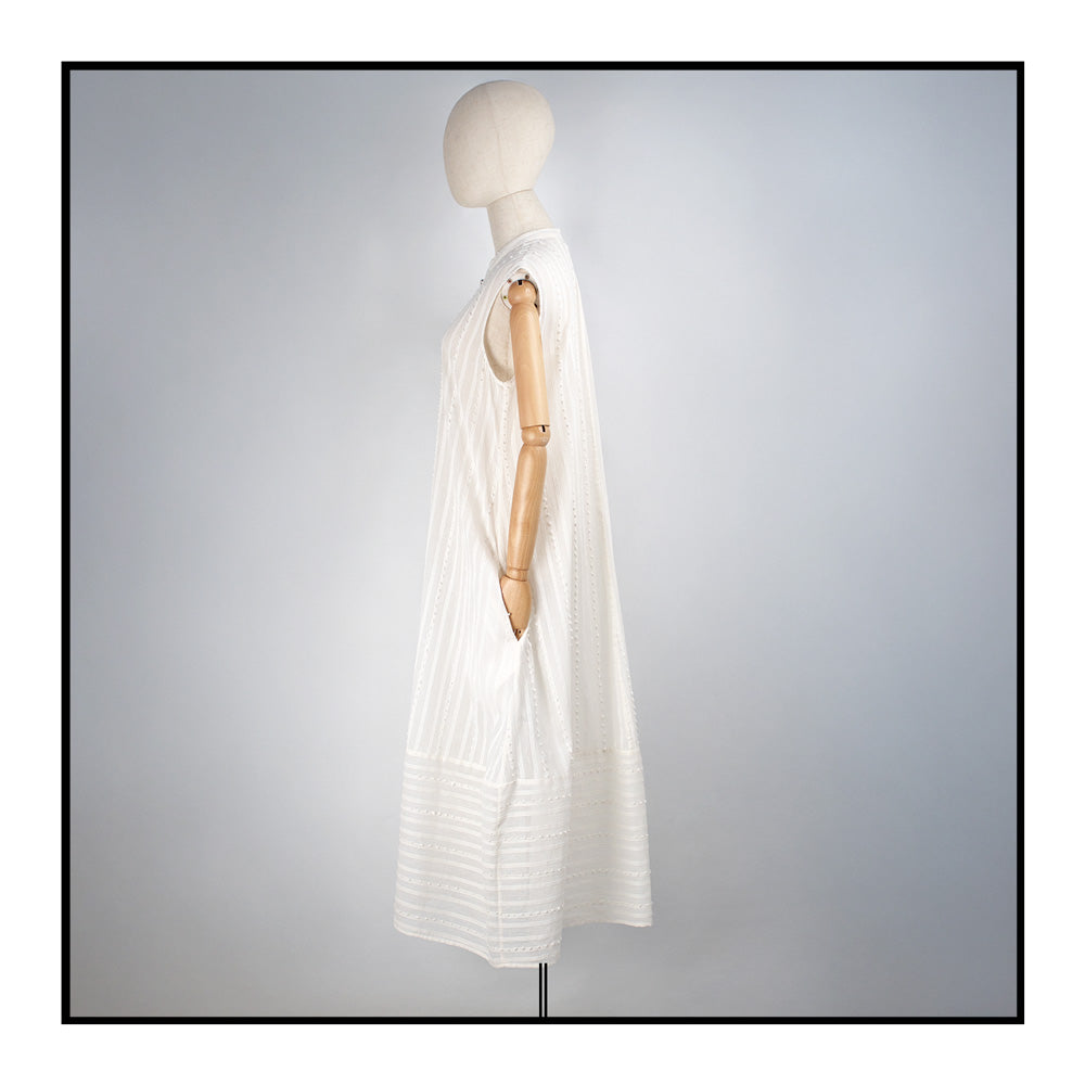 Cream sleeveless dress with a standing collar, crafted from 100% Khadi cotton handwoven in India, featuring a flowing design with hidden pockets and a matching belt for versatile styling.