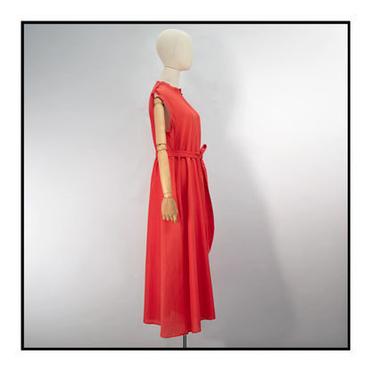 Mannequin side view of a red long sleeveless dress with a standing collar, made from 80% cotton and 20% silk, featuring Antonello Tedde's signature pom details, a flowing design, hidden pockets, and a matching belt.