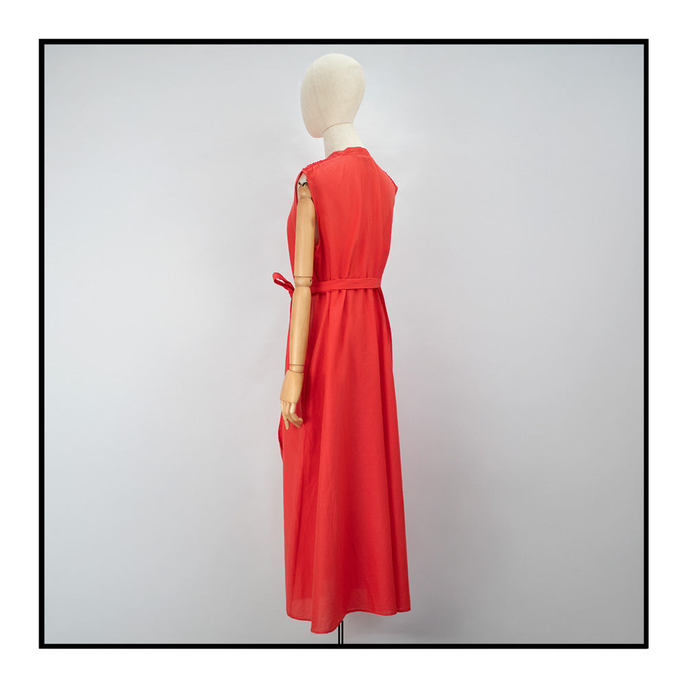 Mannequin back view of a red long sleeveless dress with a standing collar, made from 80% cotton and 20% silk, featuring Antonello Tedde's signature pom details, a flowing design, hidden pockets, and a matching belt.