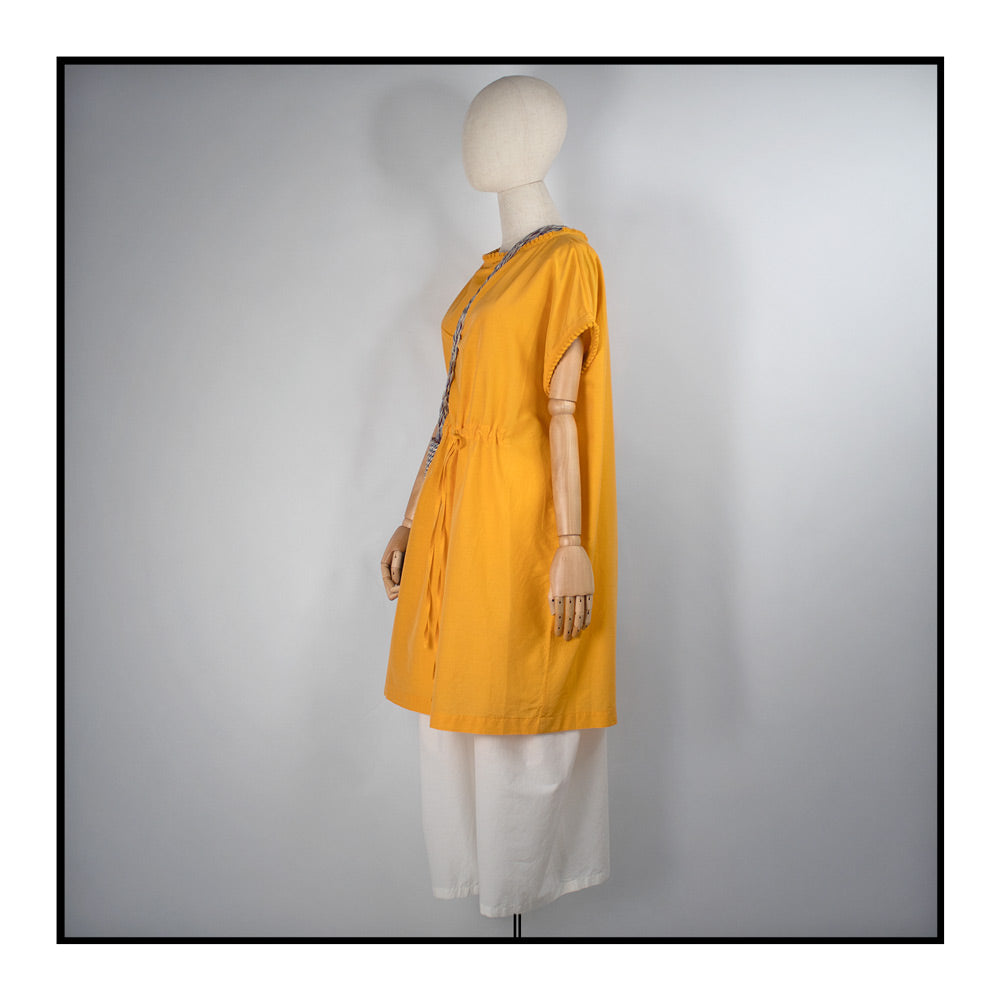 Mustard yellow cover-up dress with round collar, pom details on the collar and sleeve edges, adjustable drawstring waist belt, crafted from 80% cotton and 20% silk, designed for lightweight comfort and elegance.