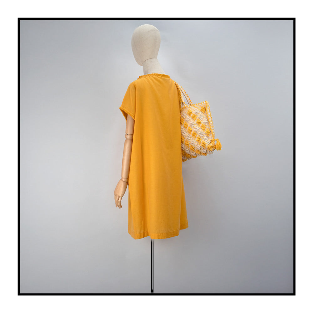 Mustard yellow cover-up dress with round collar, pom details on the collar and sleeve edges, adjustable drawstring waist belt, crafted from 80% cotton and 20% silk, designed for lightweight comfort and elegance.