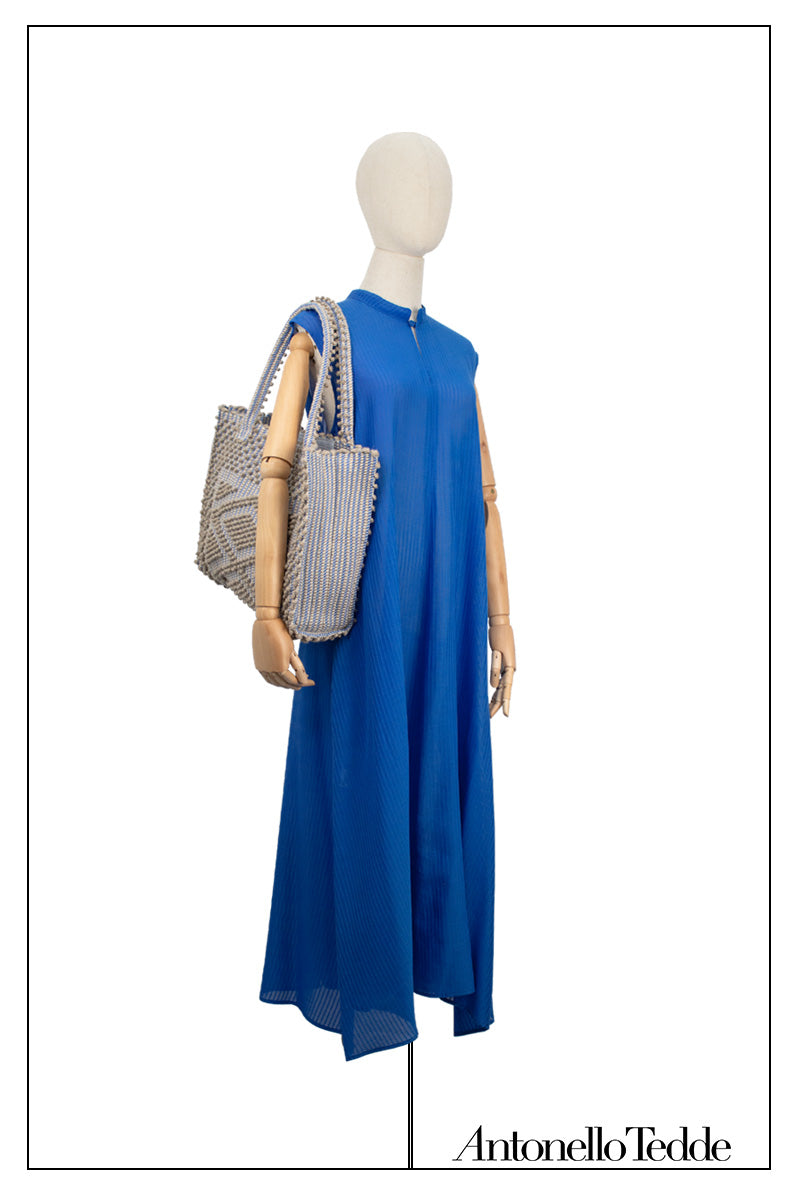 Front view of the Long Sleeveless Dress with Standing Collar with no belt styled with bag. Crafted from a luxurious blend of 94% cotton and 6% silk, this elegant dress comes in a rich marine shade, exuding timeless sophistication. The sleek, sleeveless design is adorned with stable stitch decorations, adding subtle texture and refined detail to the fabric, making it a standout piece for any occasion.